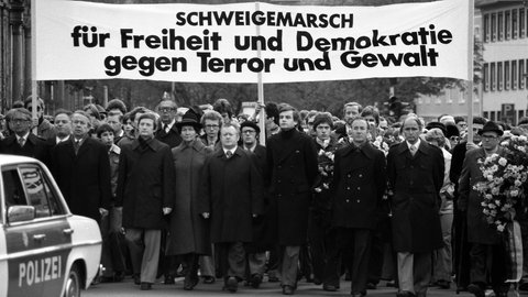 Dunkel gekleidete Menschen mit Transparent „Schweigemarsch für Freiheit und Demokratie - gegen Terror und Gewalt“