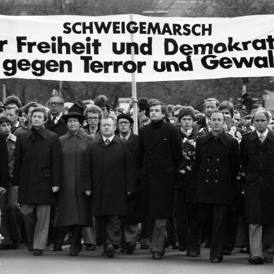 Dunkel gekleidete Menschen mit Transparent „Schweigemarsch für Freiheit und Demokratie - gegen Terror und Gewalt“