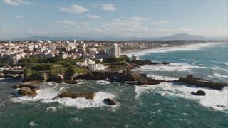 Felsige Küstenlandschaft in Biarritz mit Meer, Strand, Uferbebauung und Bergen im Hintergrund