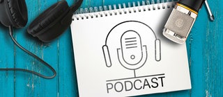 Mikrofon, Kopfhörer und ein Symbol für Podcasts auf einem blauen Tisch