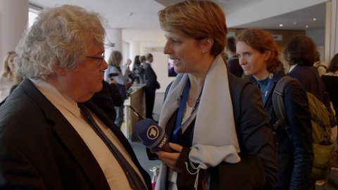 Astrid Corall mit Mikrofon interviewt einen Europa-Abgeordneten.