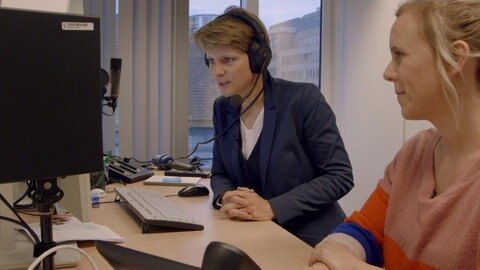 Astrid Corall mit Kopfhörern vor ihrem Monitor; neben ihr Christina Wolf.