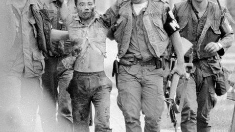 3 US-Soldaten in Uniform und mit Helmen führen einen Vietnamesen ab, der die Hände erhoben hat