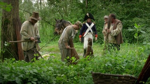 Spielszene: Männer binden im Wald Rutenbündel, in der Mitte steht Tulla.