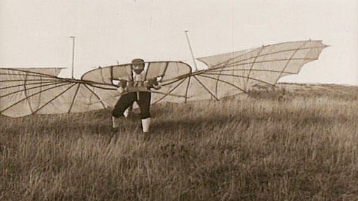 Otto Lilienthal auf einem Hügel beim Startversuch mit einem selbstgebauten Fluggerät, das vogelähnliche Flügel hat.