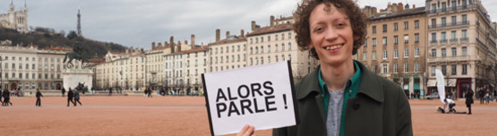 Moderator Jonas Modin steht mit einem "Alors parle!" Schild auf einem großen Platz. (Rechte: UR/WDR)