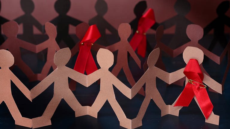 Eine Reihe von ausgeschnittenen Papierfiguren, einige tragen eine rote Schleife. (Foto: Ute Grabowsky, picture alliance / photothek)
