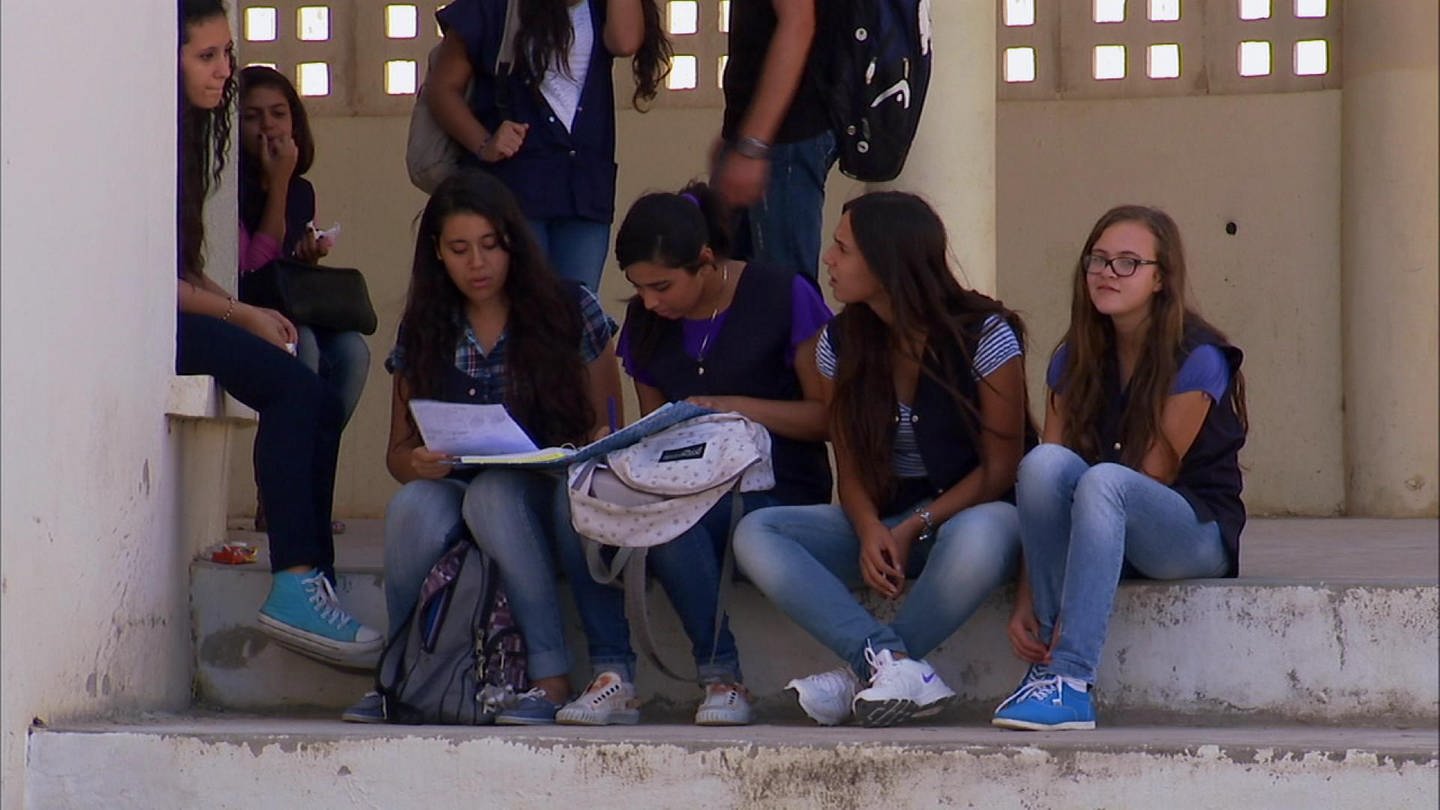 Junge Mädchen sitzen auf einer Stufe, halten ihre Rucksäcke fest, sprechen miteinander und vergleichen Hausaufgaben. (Foto: WDR - Screenshot aus der Sendung)