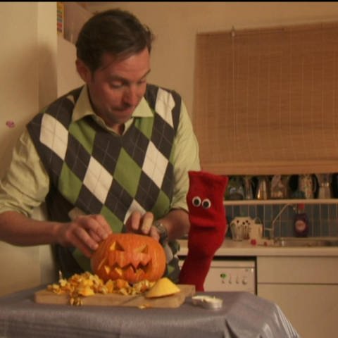 Ein Mann und eine rote Strumpfhandpuppe höhlen einen Kürbis für Halloween aus. (Foto: WDR - Screenshot aus der Sendung)