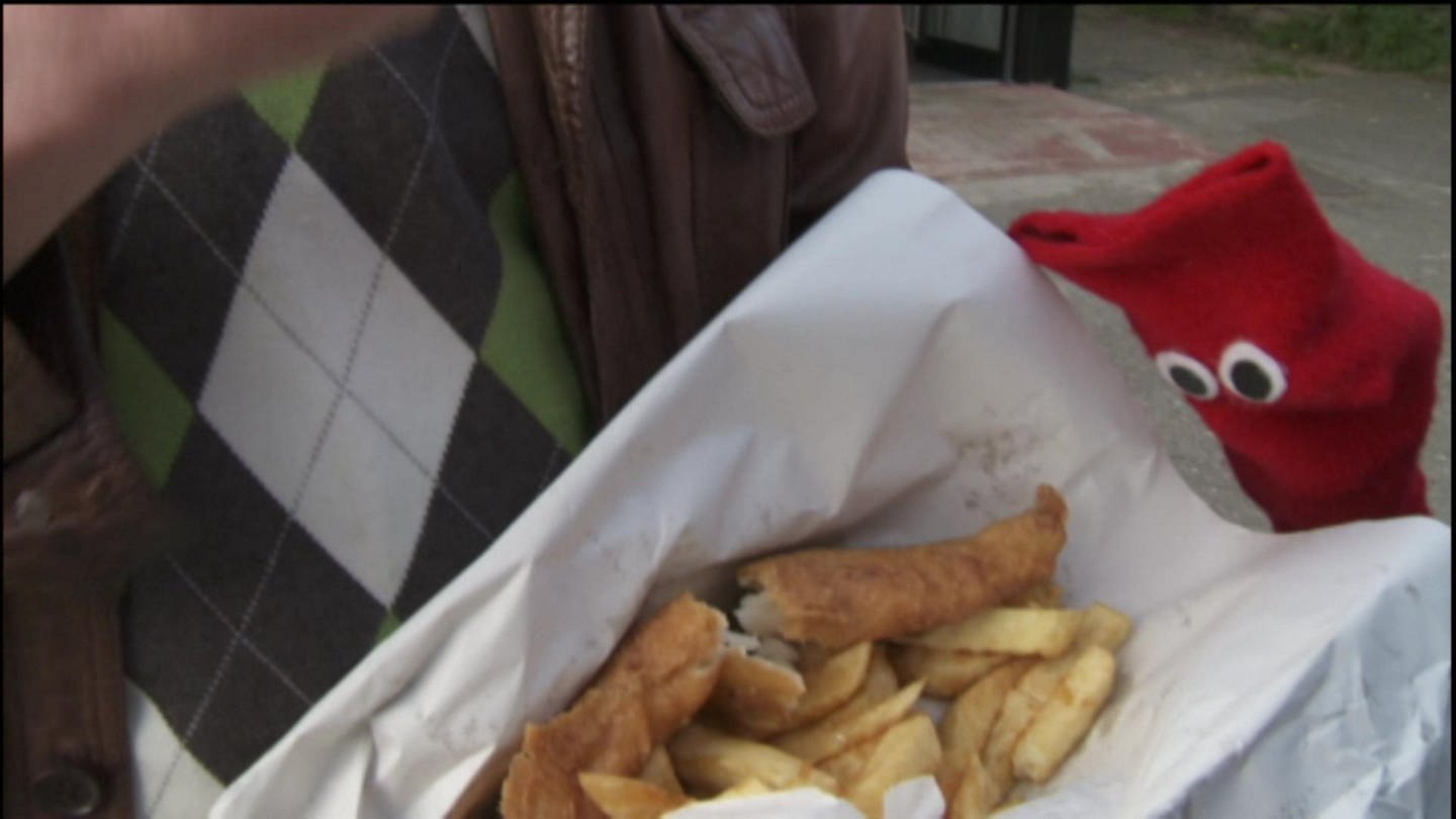 Eine Hand hält eine Portion Fish and Chips.