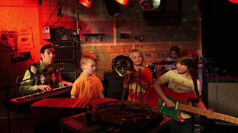 Ein dunkler Raum mit Aufnahmegeräten, Instrumenten und einer Diskokugel. In dem Raum ist eine Band: ein Mann und vier Kinder. (Foto: WDR)