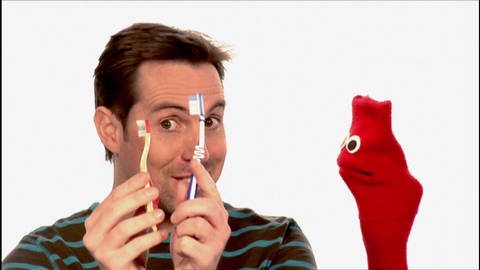 Ein Mann hält zwei Zahnbürsten hoch. Neben ihm eine rote Strumpfhandpuppe. (Foto: WDR - Screenshot aus der Sendung)