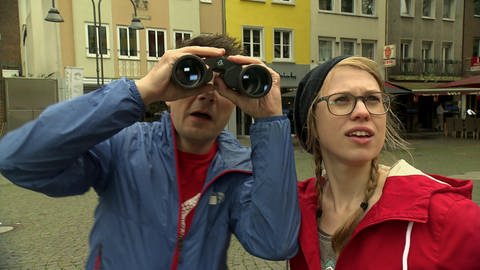 Ein Mann und eine Frau gucken suchend in den Himmel. Der Mann schaut durch ein Fernglas. (Foto: WDR - Screenshot aus der Sendung)