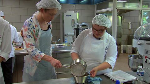 Zwei Menschen mit Kochschürze und Haarnetz in einer großen Küche. (Foto: WDR - Screenshot aus der Sendung)