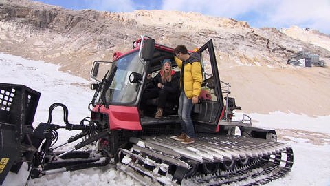 Zwei Personen in einem Schneemobil in den Bergen. (Foto: SWR / BR / WDR - Screenshot aus der Sendung.)