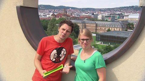 Ein Mann und eine Frau stehen vor einem runden Loch in einer Mauer, im Hintergrund eine Stadt. (Foto: SWR / BR / WDR - Screenshot aus der Sendung)