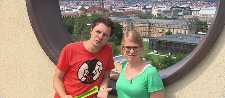 Ein Mann und eine Frau stehen vor einem runden Loch in einer Mauer, im Hintergrund eine Stadt. (Foto: SWR / BR / WDR - Screenshot aus der Sendung)