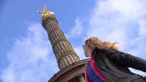 Eine Frau steht unter der Siegessäule in Berlin. (Foto: SWR / BR / WDR - Screenshot aus der Sendung)
