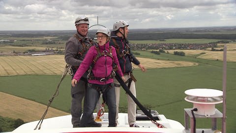Drei Personen stehen mit Klettergurten und Helmen gesichert auf einem Windrad. (Foto: SWR / BR / WDR - Screenshot aus der Sendung)