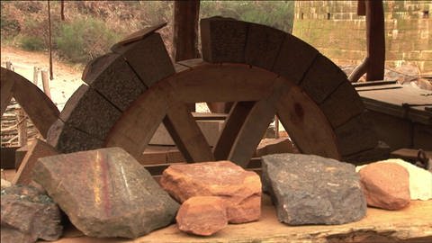 Verschieden geformte Steine auf einem Tisch und einem Holzrad. (Foto: WDR / SWR - Screenshot aus der Sendung)