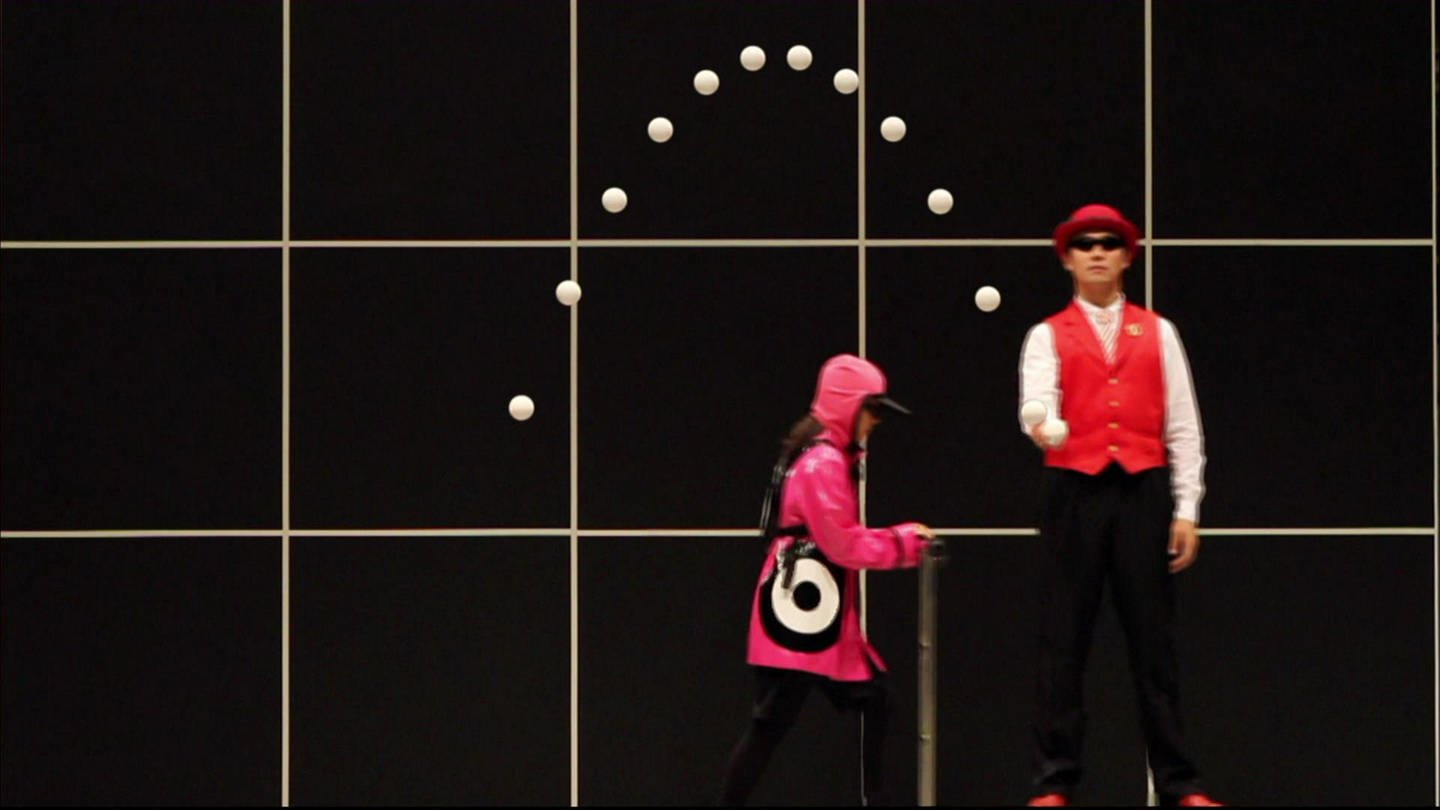 Zwei Personen stehen vor einer schwarzen Wand. Eine Person wirft einen Ball in die Höhe, seine Flugbahn ist eingezeichnet. (Foto: SWR - Screenshot aus der Sendung)