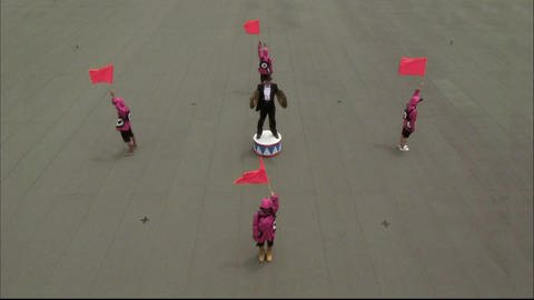 Der Auftrag:  Eine schwarz gekleidete Person mit Zylinder und zwei Becken steht auf einem Platz, um ihn herum stehen vier Personen und halten Fahnen in die Luft. Schallgeschwindigkeit messen (Foto: SWR - Screenshot aus der Sendung)