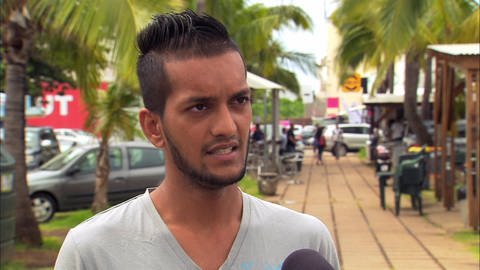 Ein junger Mann wird in einer Einkaufspassage unter Palmen interviewt. (Foto: WDR - Screenshot aus der Sendung)
