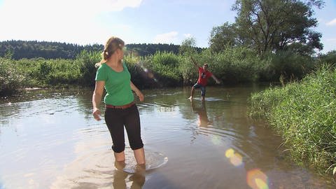 Eine Frau und ein Mann laufen barfuß durch einen Fluss. (Foto: SWR / BR / WDR - Screenshot aus der Sendung)