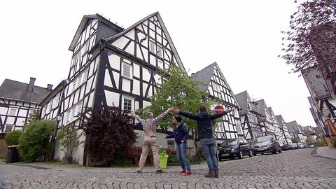 Drei Menschen stehen vor einem Fachwerkhaus. Zwei heben die Arme hoch, in der Mitte steht die dritte Person.  (Foto: WDR - Screenshot aus der Sendung)