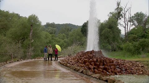 Drei Personen stehen neben der Fontäne eines Geysirs. (Foto: SWR / BR / WDR - Screenshot aus der Sendung)