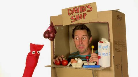 Ein Mann sitzt in einem Einkaufsladen aus Pappe. Auf einem Schild steht „David‘s Shop“.  (Foto: WDR - Screenshot aus der Sendung)