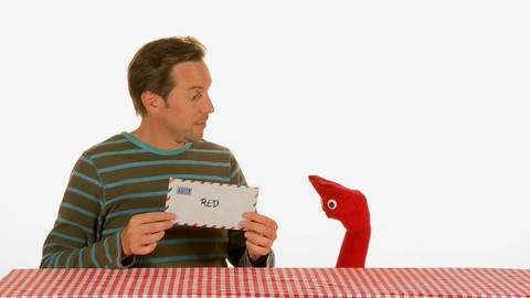 Ein Mann hält einen Briefumschlag in den Händen. Eine rote Strumpfhandpuppe schaut ihm dabei zu. (Foto: WDR - Screenshot aus der Sendung)