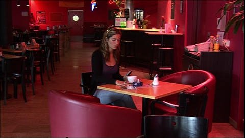 Eine junge Frau sitzt allein in einer Bar und schaut wütend auf ihr Handy. (Foto: WDR)