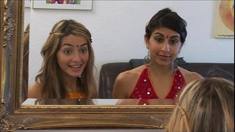 Zwei junge Frauen stehen vor einem Spiegel und sprechen miteinander, beide tragen einen Bindi. (Foto: WDR)