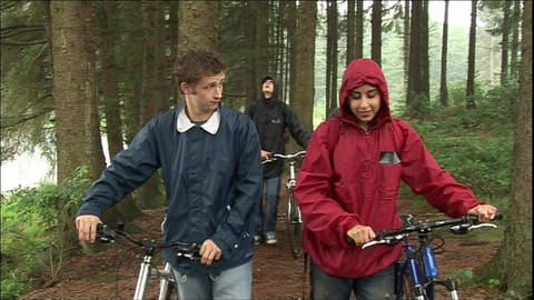 Vier junge Erwachsene schieben ihre Fahrräder durch einen Wald, es regnet. (Foto: WDR)