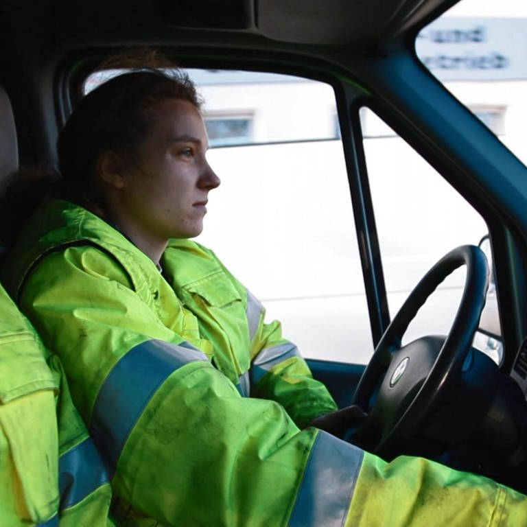 Eine junge Frau und ein junger Mann sitzen im Auto. Beide tragen neongelbe Arbeitsjacken. (Foto: WDR)