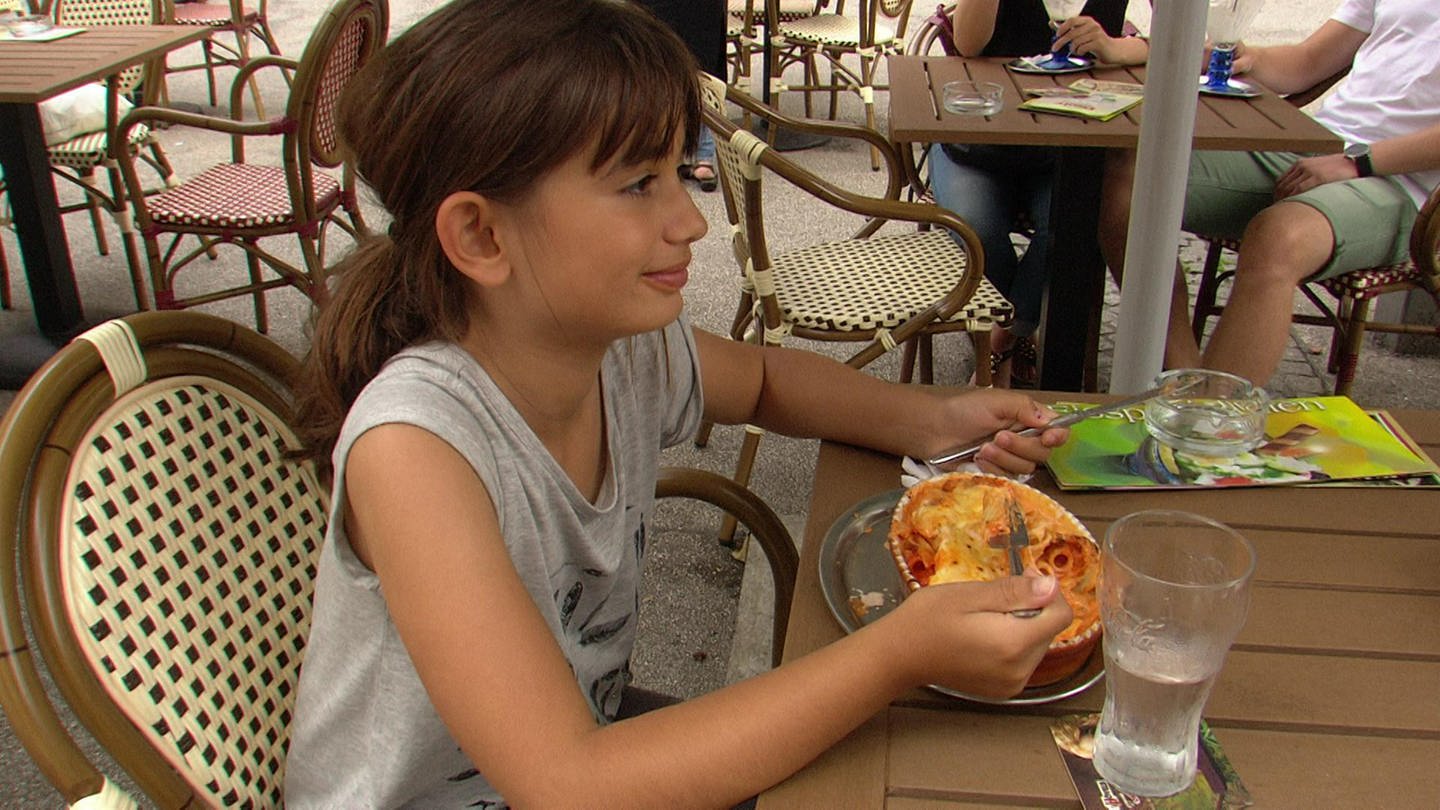 Ein Mädchen sitzt an einem Tisch im Biergarten und isst Lasagne. (Foto: WDR)