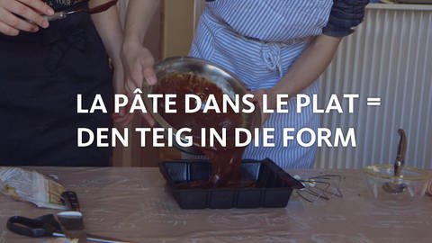 Kuchenteig wird in eine Backform gefüllt, davor der Schriftzug "La pâte dans le plat = den Teig in die Form". (Foto: WDR)