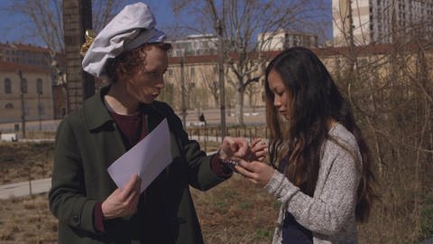 Ein junger Mann mit weißer Mütze zeigt einer Frau etwas auf einem Handy. (Foto: WDR)