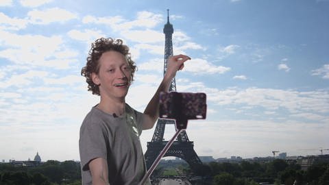 Ein junger Mann filmt sich mit seinem Handy vor dem Eiffelturm. (Foto: WDR)