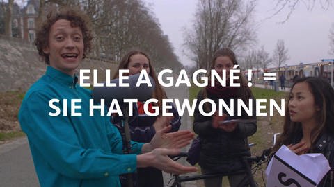 Vier Menschen stehen zusammen, vor ihnen der Schriftzug "Elle a gagné = sie hat gewonnen". (Foto: WDR)