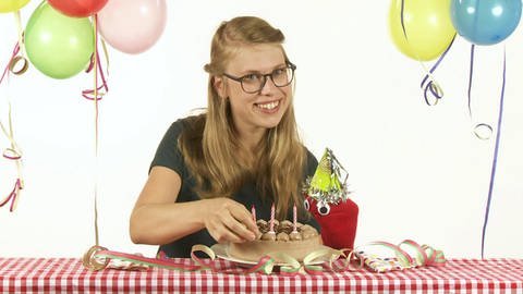 Esther und die rote Socke sitzen an einem Tisch und feiern mit Schokotorte und Luftballons Geburtstag. (Foto: WDR)