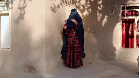 Eine Frau verhüllt sich an einer geschützten Hausecke mit der Burka (Foto: SWR)