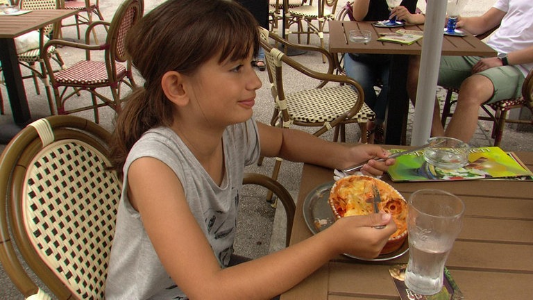 Ein Mädchen sitzt an einem Tisch im Biergarten und isst Lasagne.  (Foto: WDR)