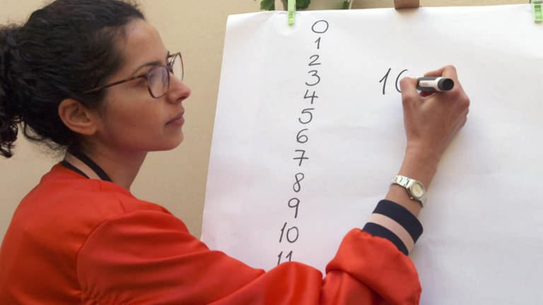 Eine Frau schreibt Zahlen an eine Tafel. (Foto: WDR)