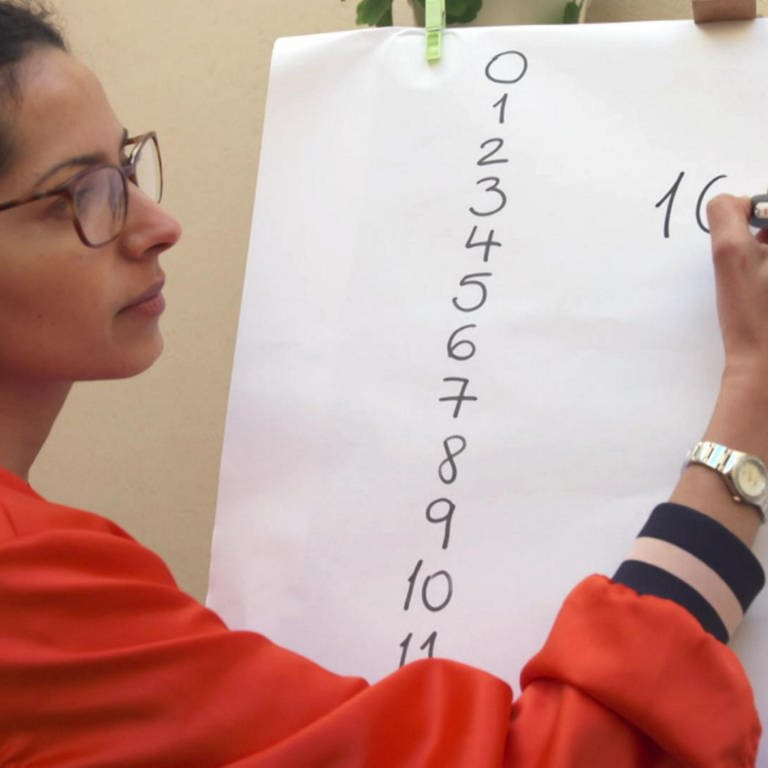 Eine Frau schreibt Zahlen an eine Tafel. (Foto: WDR)