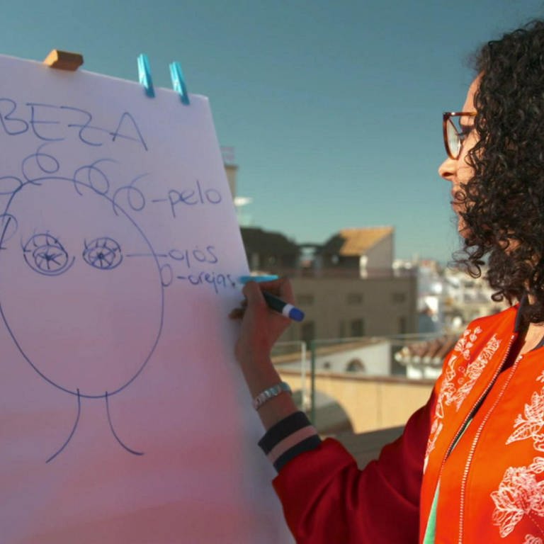 Eine Frau zeichnet einen Kopf an eine Tafel und schreibt die spanischen Namen der Körperteile auf. (Foto: WDR)