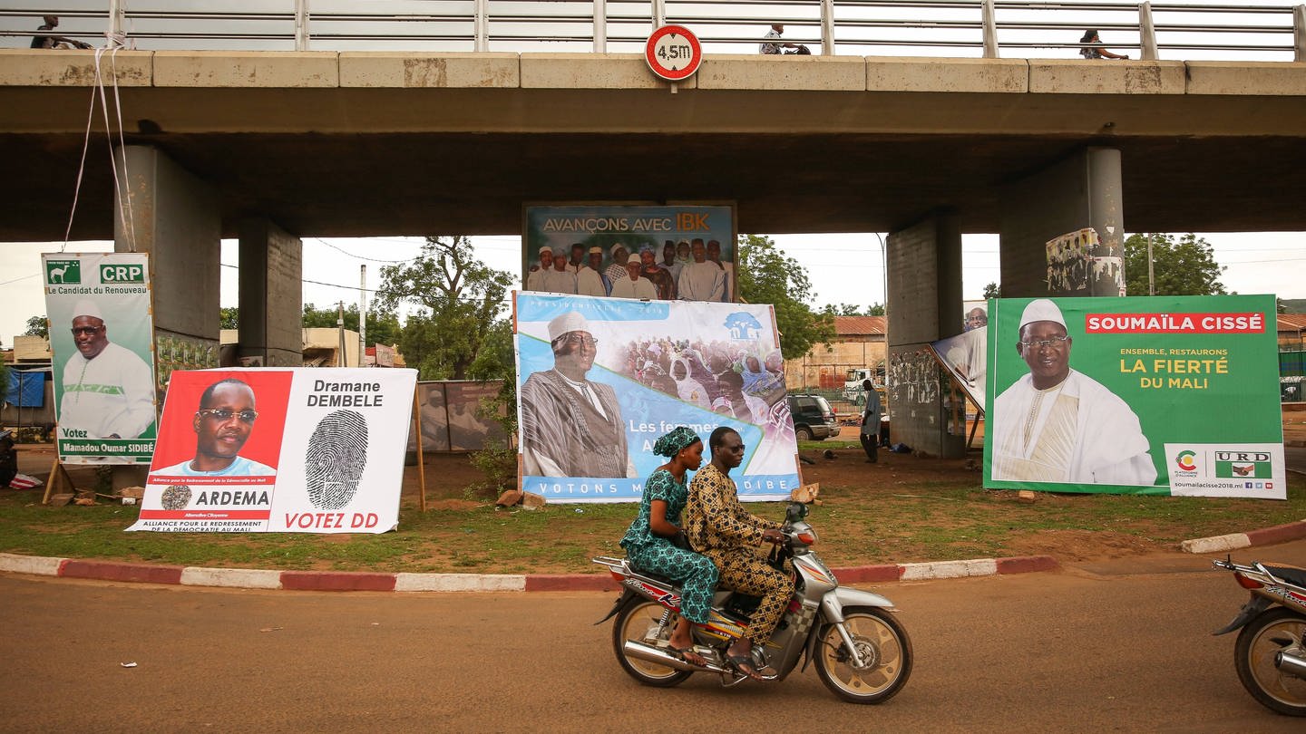 Wahlkampf in Mali für die Präsidentschaftswahl 2018 – ein junges Paar fährt auf einem Moped an Wahlplakaten vorbei (Foto: IMAGO/Le Pictorium)