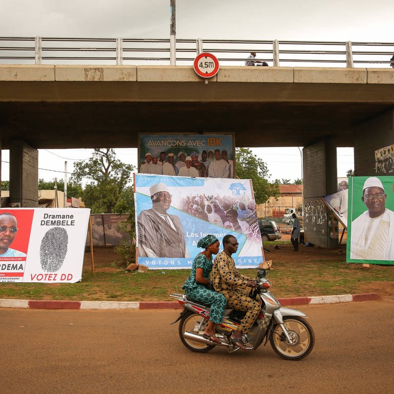 Wahlkampf in Mali für die Präsidentschaftswahl 2018 – ein junges Paar fährt auf einem Moped an Wahlplakaten vorbei (Foto: IMAGO/Le Pictorium)