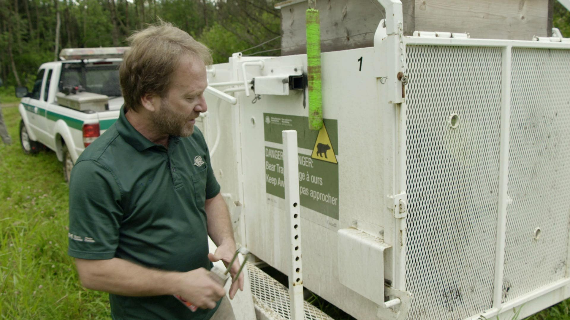 Ein Biologe steht neben einem Käfig, in dem ein Braunbär gefangen wurde. Er hält einen Schlüssel in der Hand. (Foto: WDR)